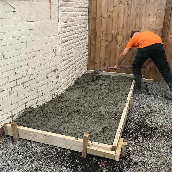 Engineer levelling wet concrete inside timber shuttering for a new oil tank base