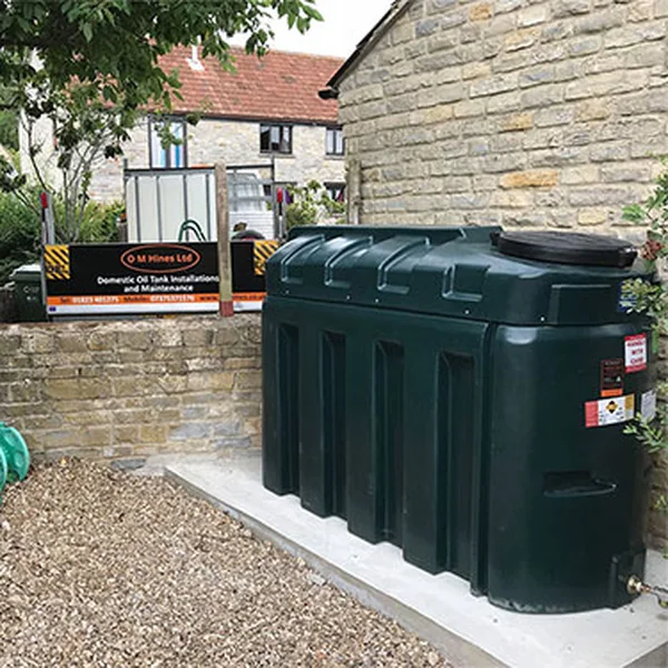 New green bunded oil tank installed on a fresh concrete base beside a stone wall